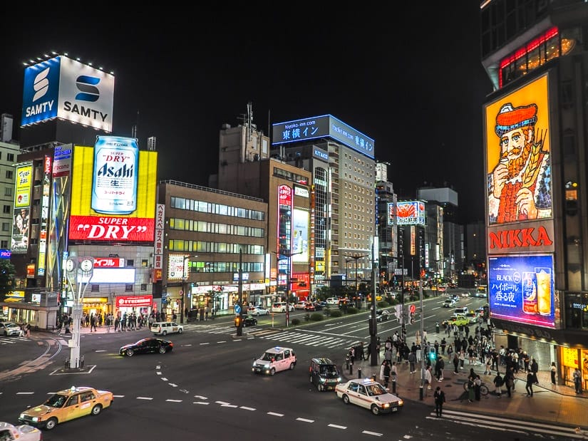A busy intersection in Sapporo at night, with famous Nikka whiskey neon sign on the left and Asahi beer sign on the right