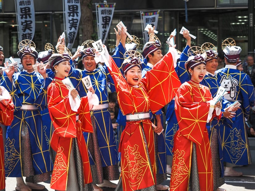 Some Japanese dancers in red and blue costumes looking excited on the street