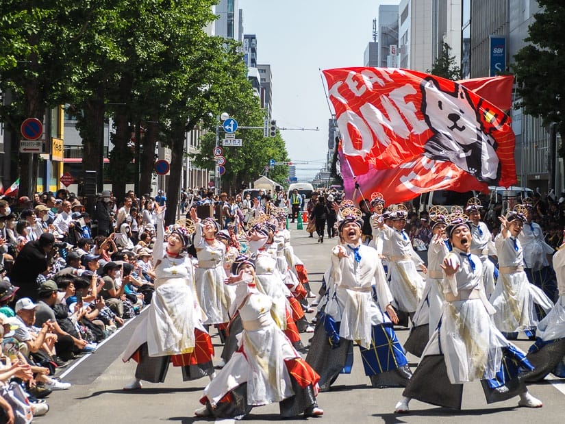 Some Japanese dancers in white costumes on the street with crowds of spectators to the side