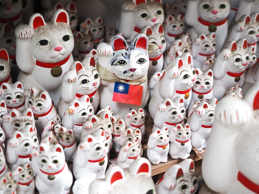 A collection of white beckoning arm cat statues with one of them wearing a little Taiwan flag on its neck