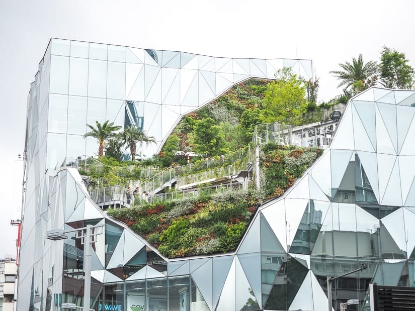 A tall glass building with large garden patio carved into the side of it