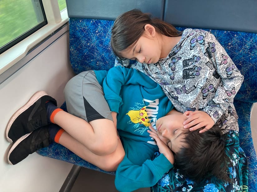 A young brother and sister sleeping on a train seat