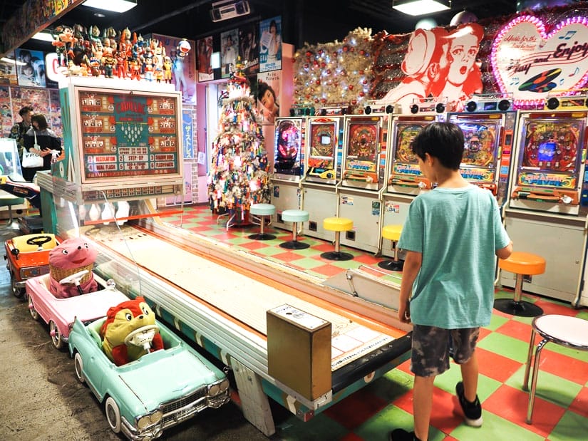 A boy standing at a children's size bowling lane with vintage toys all around