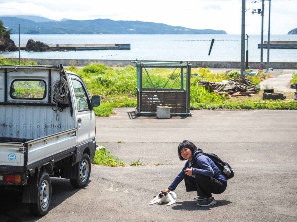 Nick Kembel's wife Emily kneeling down and petting a cat on the pavement beside a harbor with sea and islands visible in the background