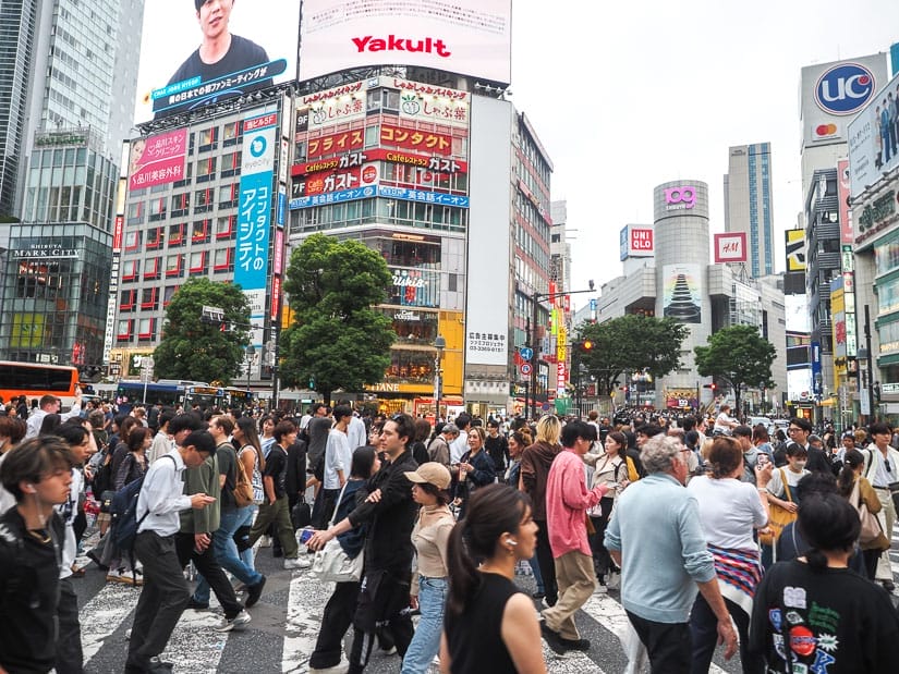 A crowd of people walking in all directions and Shibuya Crossing, with buildings with many Japanese signs behind