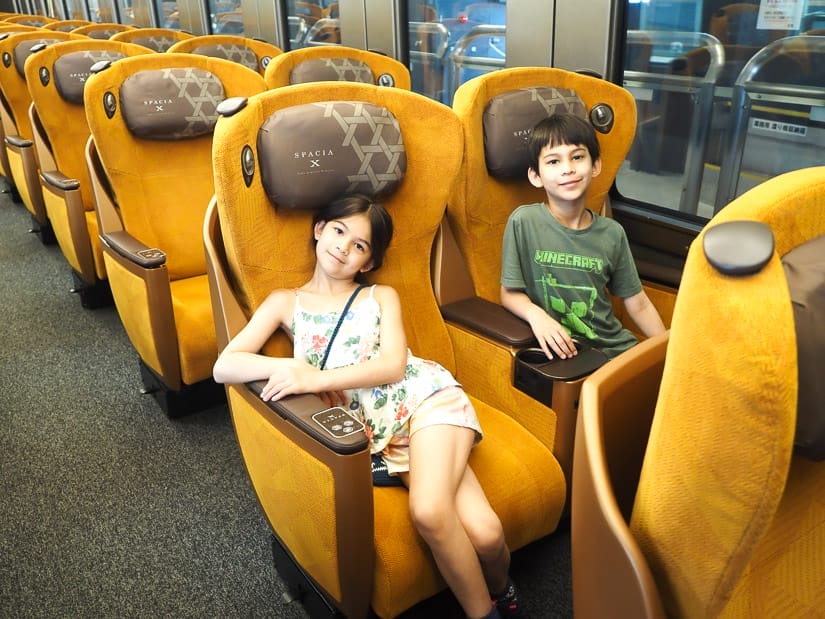 Two kids sitting on very comfortable looking orange train seats