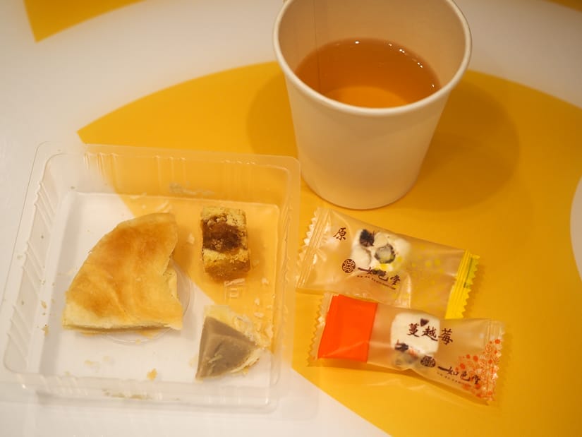 Some sample slices of Taiwanese pastries on a table with little paper cup of tea