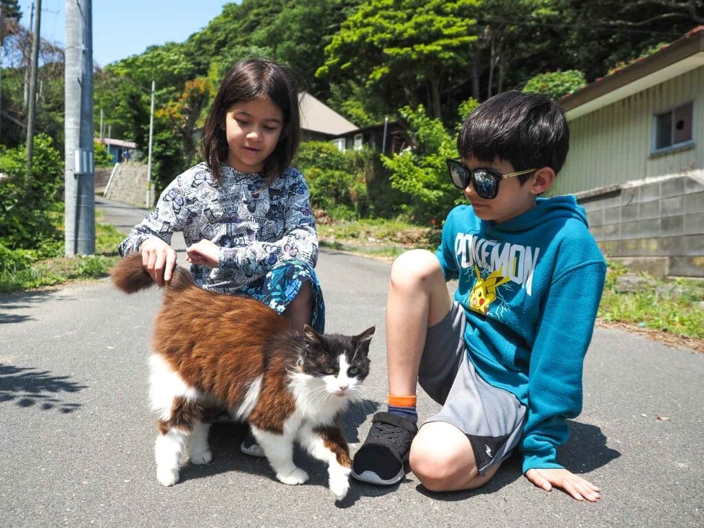 Nick Kembel's son and daughter kneeling down on a road and petting a poofy cat