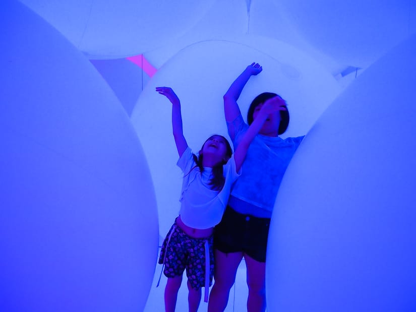 A mother and daughter standing between huge bouncy balls in a room with blue lights