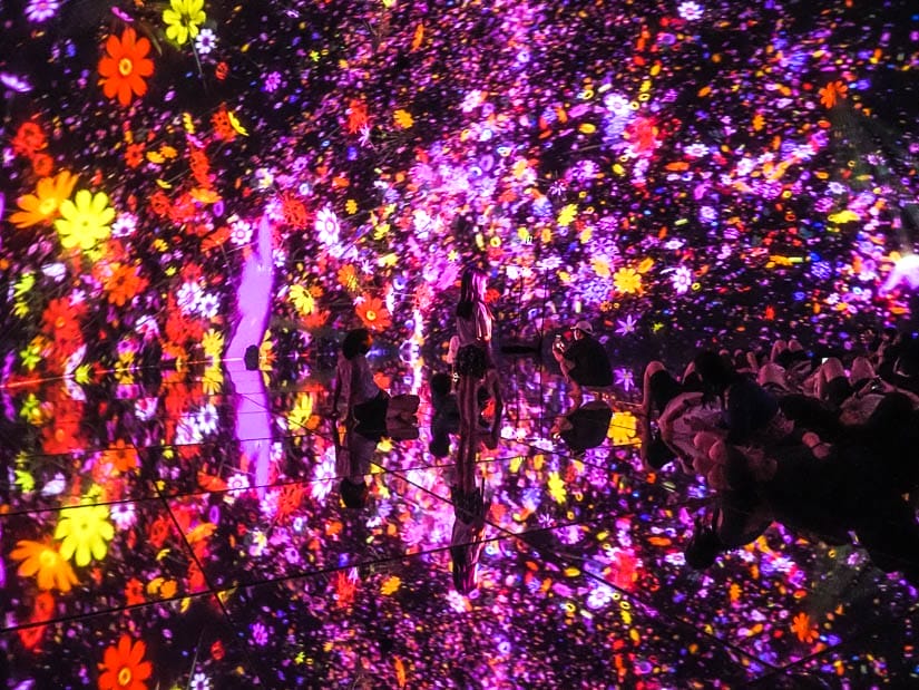 A room filled with light patterns reflecting on the walls and floor with some people hardly visible sitting on the ground enjoying it