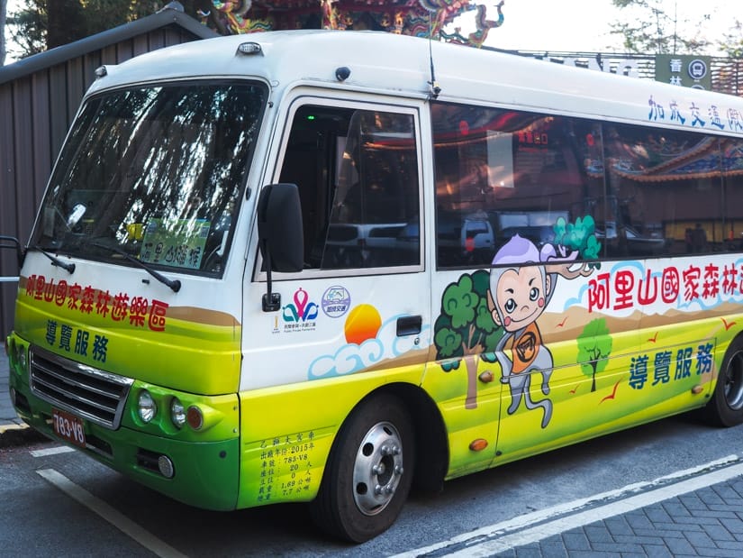 A green and white Alishan electric shuttle bus with cute characters on the side