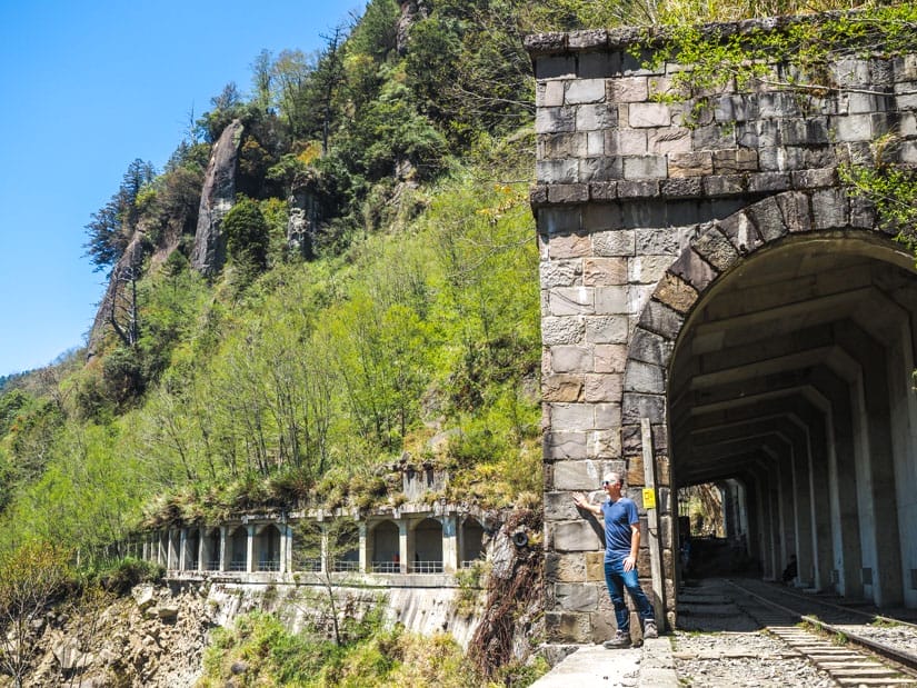 Nick Kembel standing at the entrance to a train tunnel on the side of a mountain