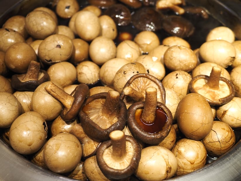 A large vat filled with brown tea eggs and mushrooms