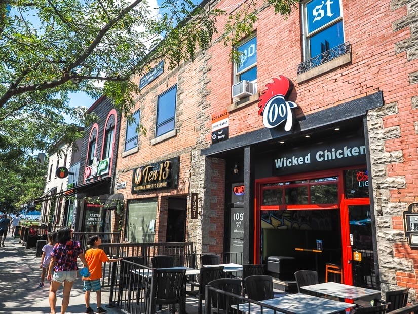 A woman and two kids walking down a sidewalk with brick buildings containing restaurants to their right