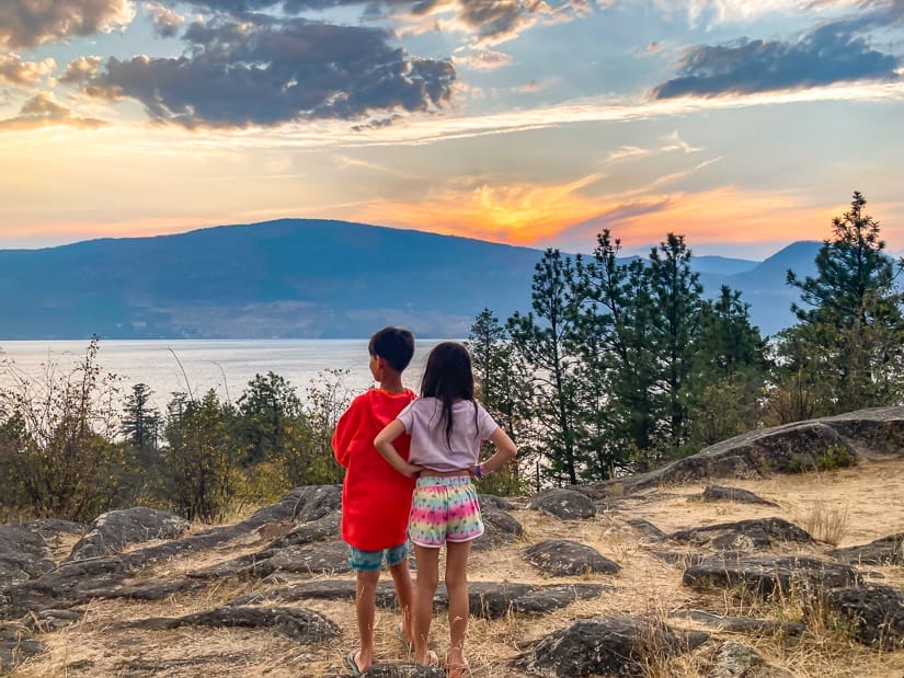 Two kids shot from behind as the watch the sunset over the lake in front of them