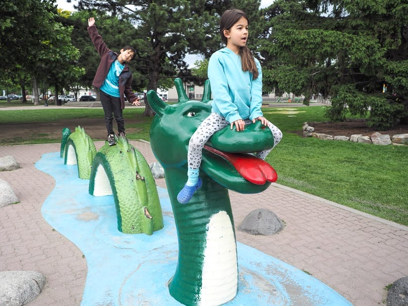 Two kids sitting and standing on top of a statue of the Ogopogo in Kelowna