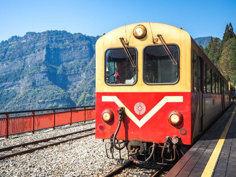 An red and yellow Alishan Forest Railway train parked at Erwanping station, with mountain in background