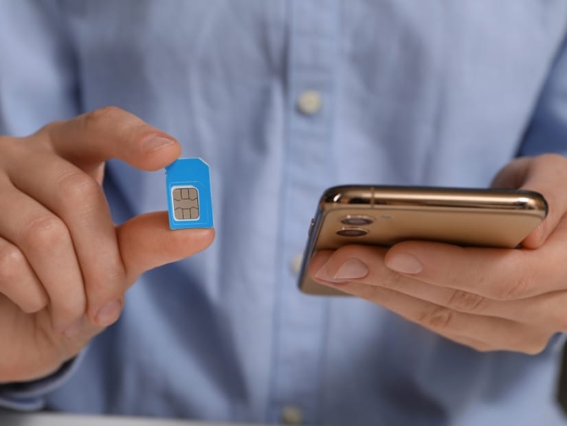 Close up of a man's hands, with one holding up a little SIM card and the other his phone
