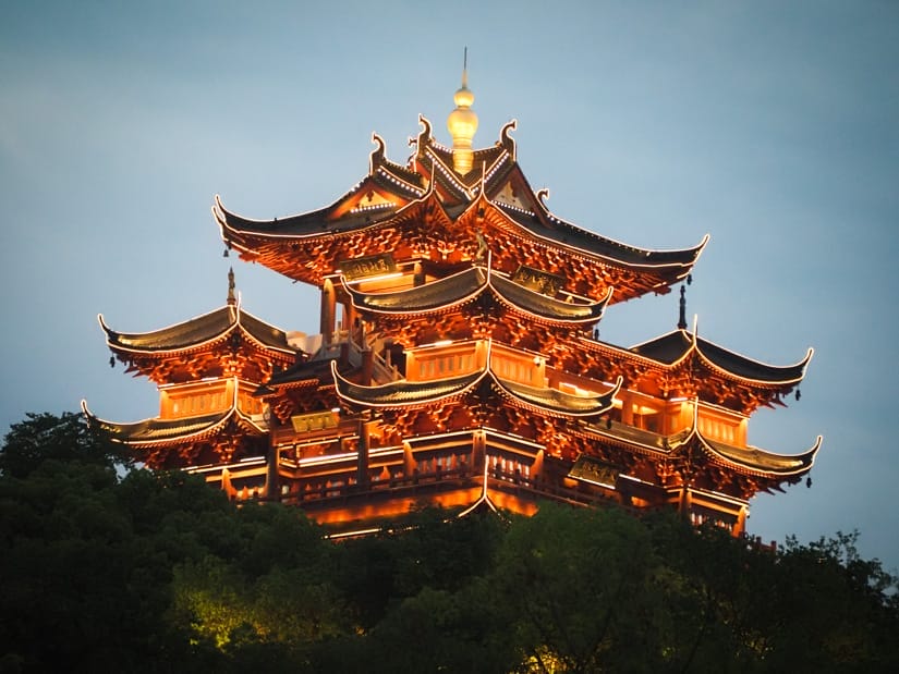 A tall Chinese pavilion on top of a hill and lit up at night