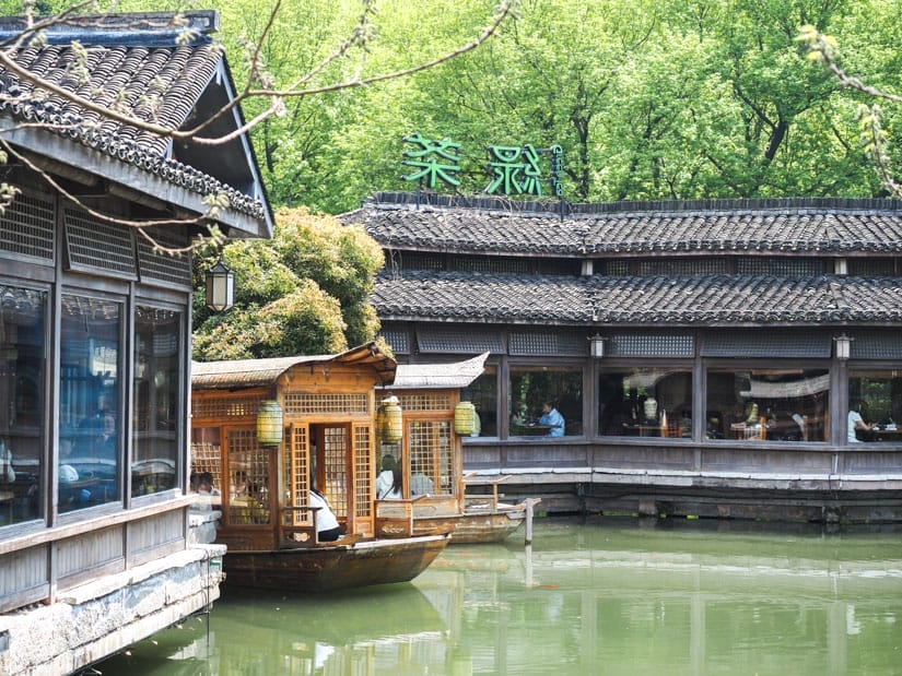 A restaurant built on a pond, with two long buildings and some covered boats with diners on them