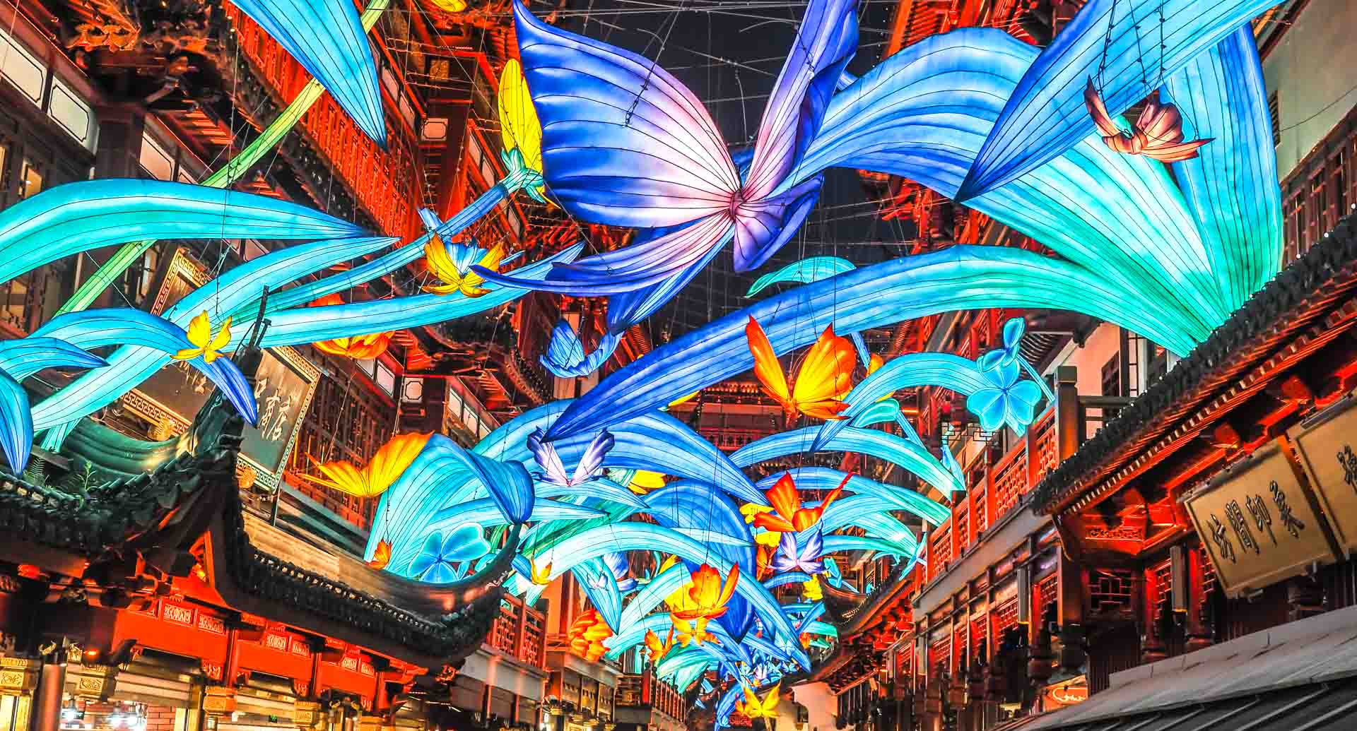Some butterfly shaped lanterns between two rows of traditional Chinese buildings lit up at night in Yuyuan Garden, Shanghai