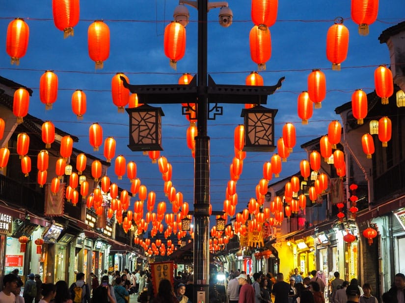 Looking down a pedestrian shopping street at night, with crowds of shoppers and rows of red lanterns hanging above