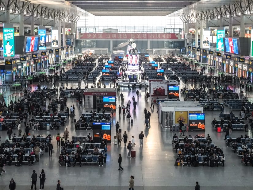 From from above looking down on the HSR terminal of Shanghai Hongqiao station with many passengers sitting or walking around and boarding gates lining either side