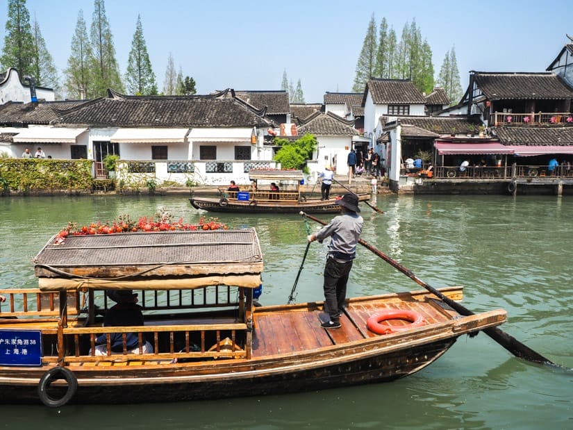 A canal with traditional Chinese boat going by with guy standing on the front pushing it along