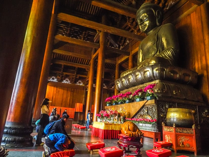 A young boy and a few other people kneeling down and prostrating before a large Buddha statue inside Jing'an Temple