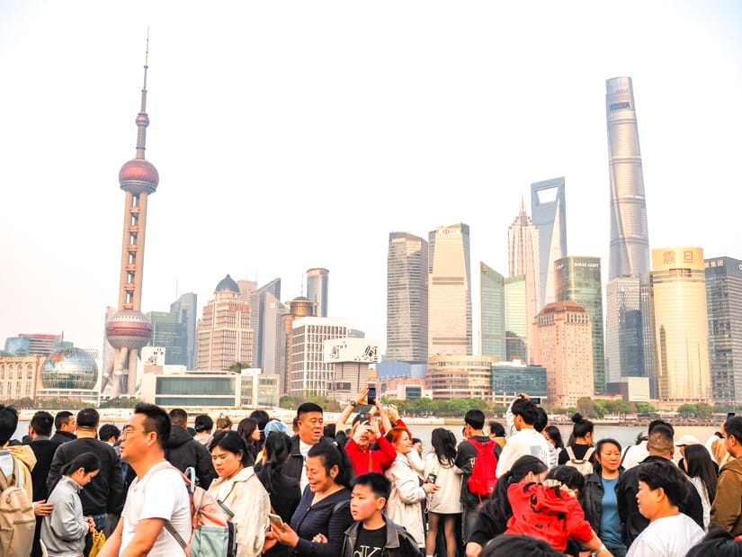 A crowd of Chinese people next to a river with view of Pudong's skyscrapers across the river