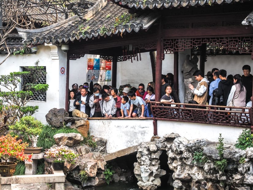 A crowd of Chinese visitors in a open hallways of Yu Garden looking out at a pond