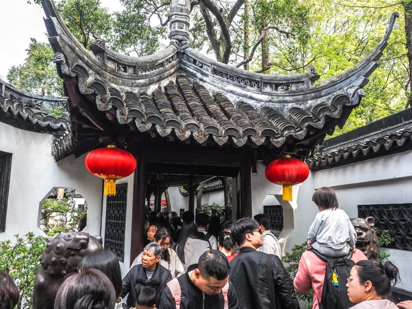A crowd of Chinese visitors squeezing through a traditional gate inside Yu Garden, with one of them carrying a toddler on his shoulders