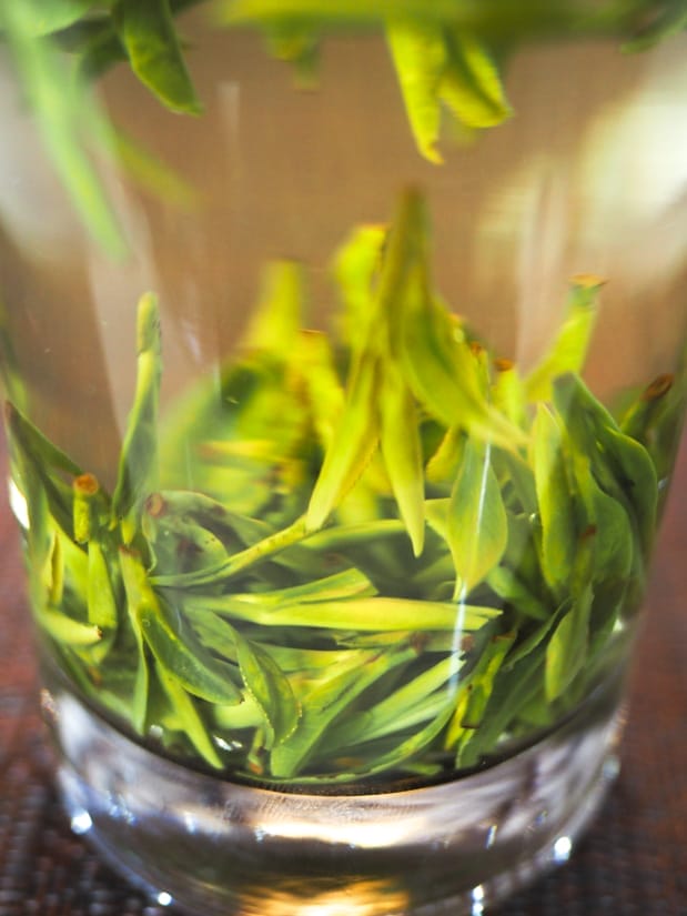 A transparent glass with jade green leaves sinking to the bottom