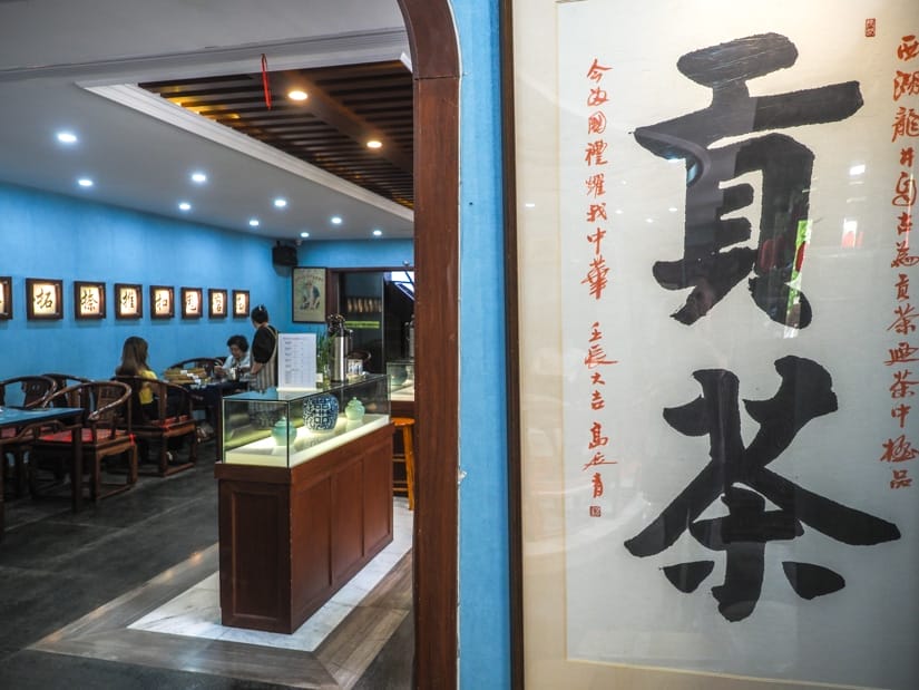 Looking into a teashop in Longjing, with Chinese characters on the wall on the right and a room inside of the left with local customers checking the teas