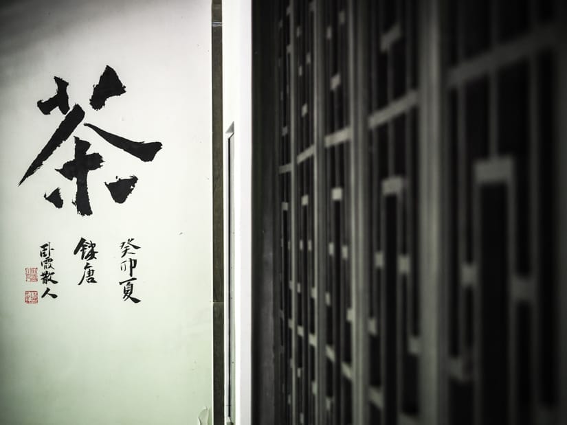 Looking down the outer black wall of a temple at a white sign with the Mandarin character for tea in black