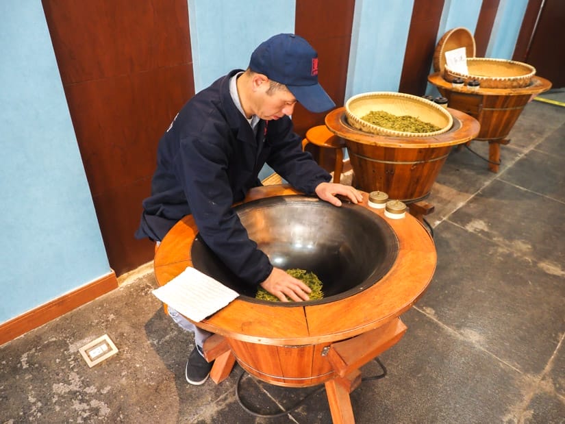 A Chinese man hunched over using his hand to move a pile of Longjing tealeaves around in a roasting pan
