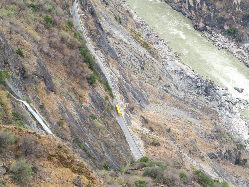 Looking down on a yellow bus far below as it drives along the river deep in Tiger Leaping Gorge