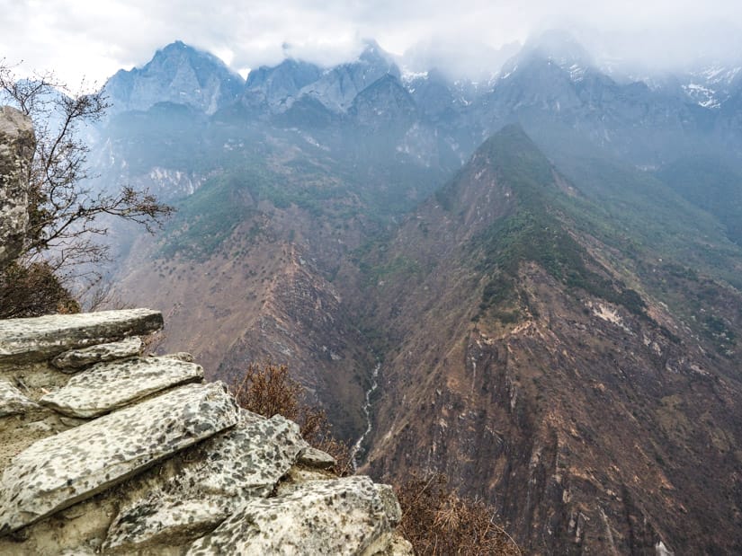 A rocky trail on the edge of a cliff looking down into Tiger Leaping Gorge