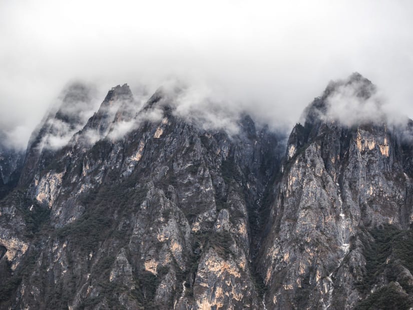A row of rocky mountain peaks with clouds around their tops