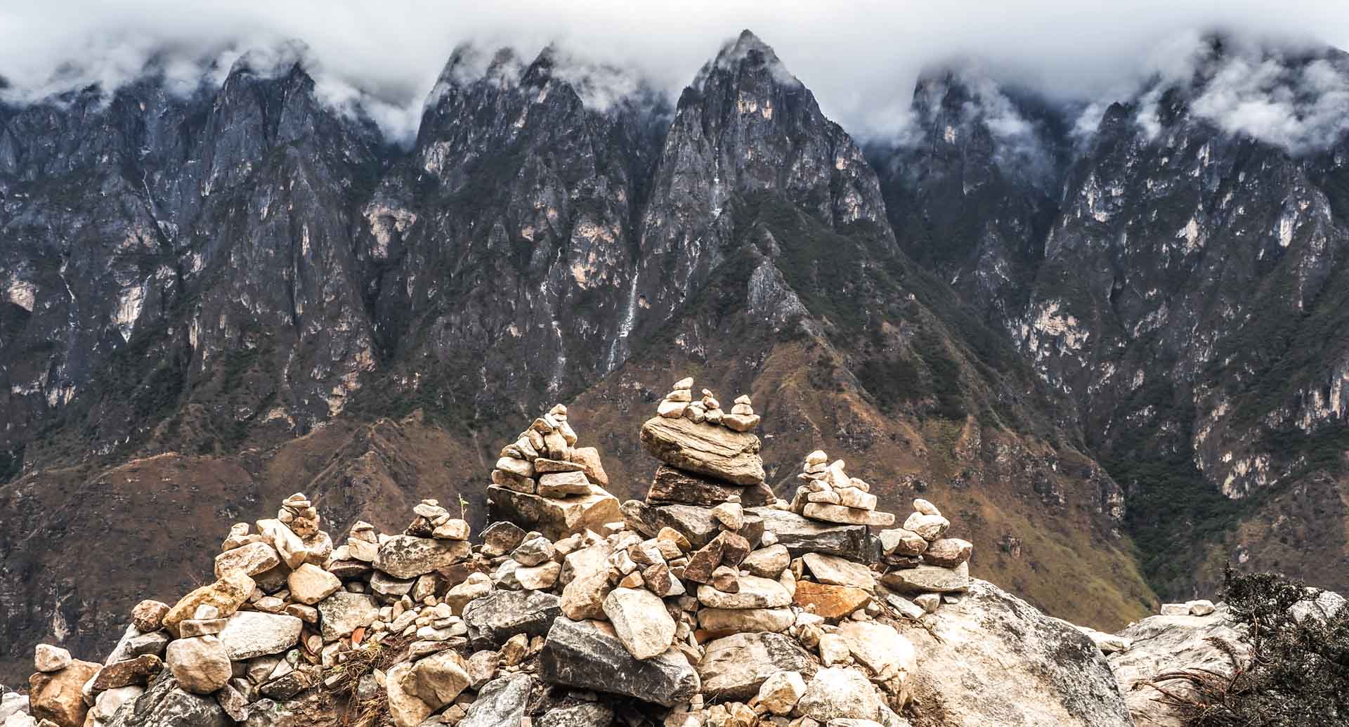 Some rock piles in the foreground with wall of cloud-topped mountains in Tiger Leaping Gorge in the background