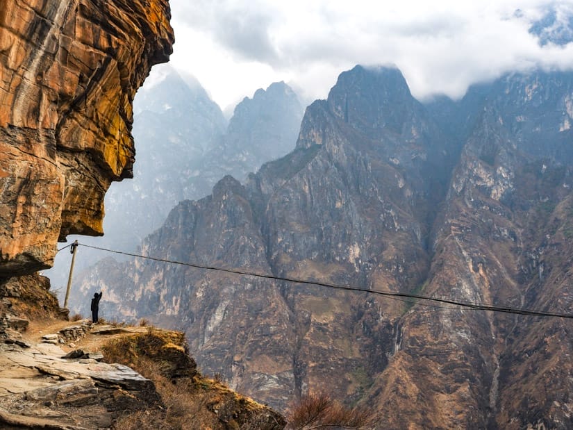 A trekker standing out on the edge of a cliff at a sharp turn in the trail through Tiger Leaping Gorge