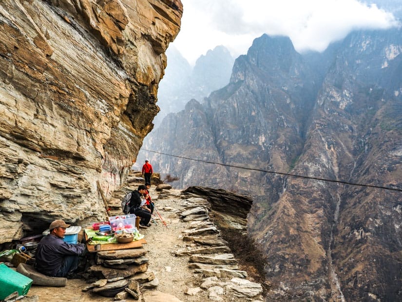 Some Chinese food vendors on the side of a narrow trail around a cliff in Tiger Leaping Gorge
