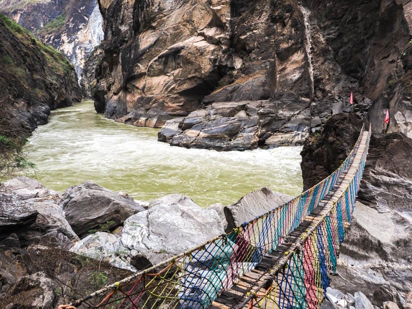 A colorful wood and rop bridge to a huge boulder by the river in Tiger Leaping Gorge, with view down the narrow gorge on the left side