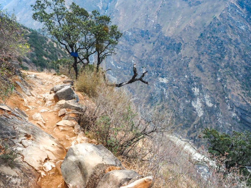 Tiger Leaping Gorge trail with a glimpse of a parking lot with cars parked in it by the river far below