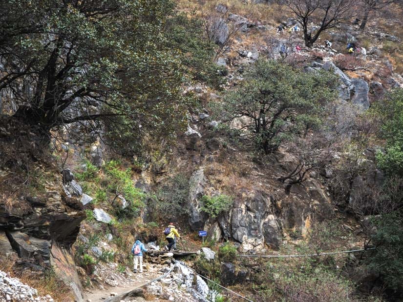 Some trekkers climbing towards and steep hill, with others visible on the trail high up on the hill