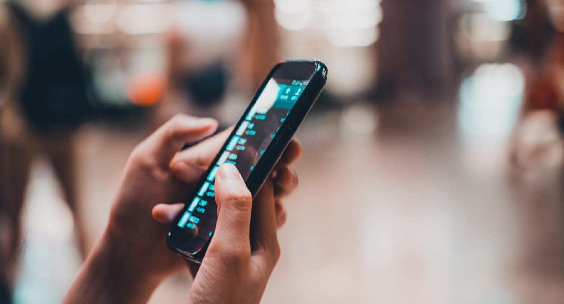 Close up of a persons hands using a cell phone in a busy public place